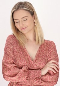 Rózsás mintás anyagú ruha hosszú ujjal és rugalmas mandzsettával. A ruha mély V-nyakkivágással és puha, természetes eséssel rendelkezik.