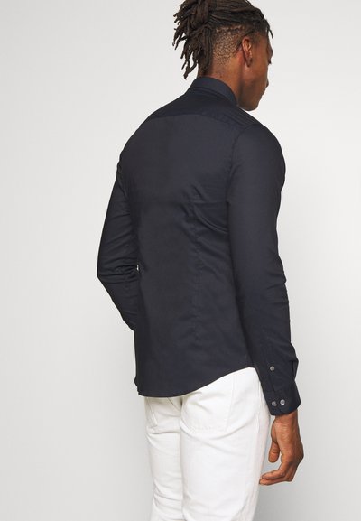 Navy blue button-up shirt with a straight hem, fitted design, and long sleeves. Features two-button cuffs and a smooth texture.