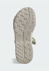 Μπεζ σόλα παπουτσιού με υφασμένο ανάγλυφο σχέδιο πέλματος, που περιλαμβάνει συνδυασμό γωνιακών και αστεροειδών σχημάτων για πρόσφυση. Περιλαμβάνει πράσινο λουράκι στη φτέρνα.