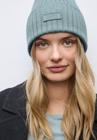 Světle modrý pletený čepice s vertikálním žebrováním a předním nášivkou s textem "COLORFUL" v obdélníkovém designu. Měkká textura.