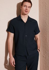Marineblauw overhemd met korte mouwen en knopen, met een geribbelde textuur en een notch-kraag, gecombineerd met bijpassende broek. Glad stof, casual ontwerp.