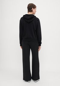 Črna sweatshirt s kapuco, sproščenega kroja in rebrastim robom. Ujeman z širšimi črnimi hlačami in belimi supergami.
