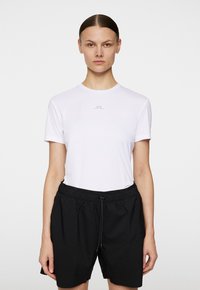 Vit t-shirt med kort ärm och rund halsringning samt en subtil grå logotyp, i kombination med svarta shorts med elastisk midja. Slät textur och enkelt mönster.