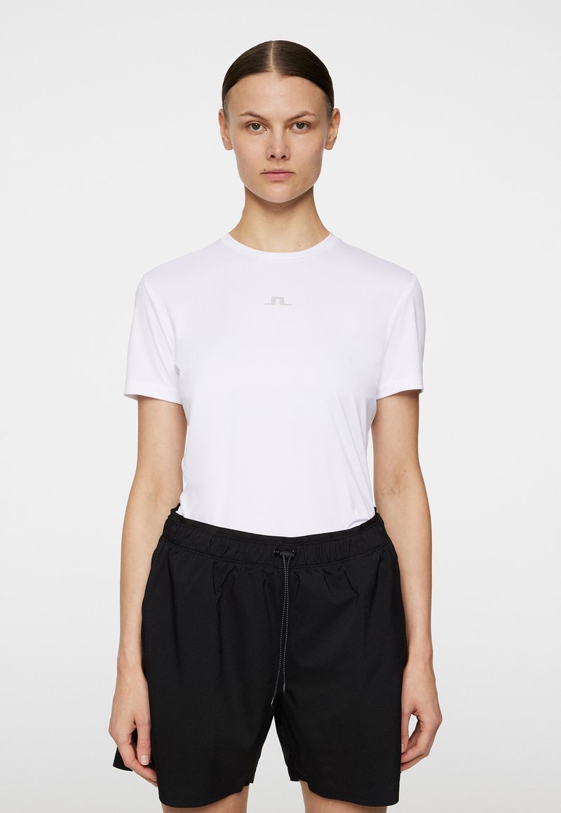 T-shirt bianco a maniche corte con collo rotondo e logo grigio discreto, abbinato a pantaloni corti con cintura elastica nera. Texture liscia e design semplice.