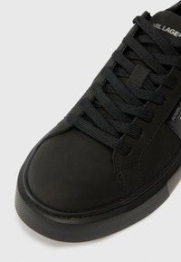 Sapatilha baixa preta com sola grossa, atacadores texturizados pretos e a marca "Karl Lagerfeld" na lateral e na língua.
