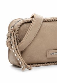 Borsa a tracolla in pelle beige con superficie texturizzata, dettagli intrecciati e borchie metalliche sulla tracolla. Include una chiusura a zip e una patch con il logo.