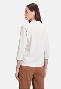 Top bianco a coste con maniche tre quarti e scollatura rotonda, abbinato a pantaloni marroni. Il tessuto ha una finitura testurizzata.