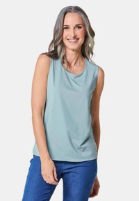 Top senza maniche di un azzurro chiaro in morbido tessuto, caratterizzato da un colletto rotondo e una caduta fluida, abbinato a jeans blu. Design semplice, senza fantasie.