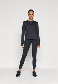 Top sportiv negru cu mâneci lungi, guler rotund și logo-ul Nike, asortat cu colanți negri și pantofi sport negri.