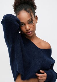 Pull en maille bleu marine surdimensionné avec large encolure dégagée et poignets côtelés. Matière texturée avec une coupe décontractée.