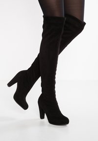 Black over-the-knee boots in soft suede, featuring a high heel, slim fit, and smooth texture. No visible hardware or patterns.