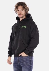 Felpa nera con cappuccio in cotone, dotata di tasca a marsupio frontale. Testo del logo verde "PROPAGANDA" sul lato sinistro del petto. Maniche lunghe, vestibilità standard.