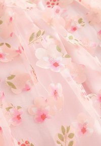 Tissu rose transparent avec un motif floral complexe comprenant des fleurs roses claires et foncées, des feuilles vertes et des accents de broderie délicats.