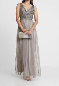 Long, gray evening gown with a V-neck, embellished bodice, and flowing chiffon skirt. Includes a silver sequined clutch, worn with open-toe shoes.