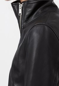 Svart läderjacka med hög krage och silverfärgad dragkedja, som visar en slät textur och en figursydd design.