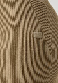 Rjava rebrasta tkanina z teksturirano površino in majhnim logotipom. Tkanina ima navpične črte in prilegajoč dizajn.