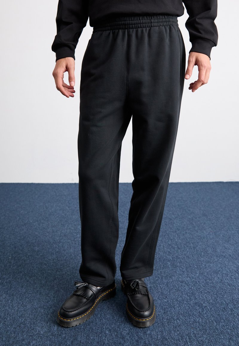 Sorte sweatpants med elastisk talje, sidelommer, lige ben-design og subtil tekstur, parret med sorte sko med kvaster.