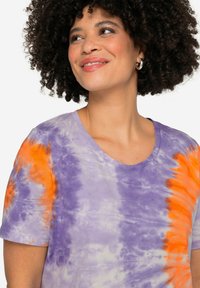 Paarse en oranje tie-dye T-shirt met een ronde halslijn en korte mouwen, gemaakt van zachte stof met een gestructureerd patroon.