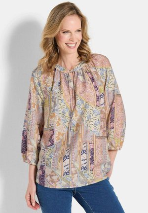 Leichte, mehrfarbige Bluse mit floralen und geometrischen Mustern, Kordelzug am Hals und Dreiviertelärmeln, kombiniert mit Jeans aus Denim.