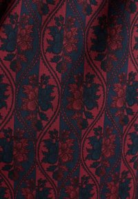 Červená a námorníckomodrá kvetinová látka s opakujúcim sa vzorom tmavých obrysov a zakrivených tvarov, prezentujúca textúrovaný, tkaný vzhľad.