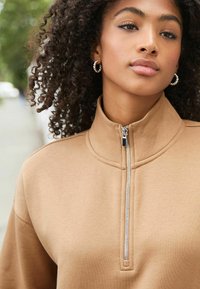 Tanha zip-up sweatshirt met een hoge kraag en een zachte textuur. Voorzien van een zilveren rits en een relaxte pasvorm, gedragen met zilveren creolen.