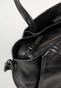 Zwarte leren handtas met zichtbare handvatten en een gedeeltelijk geopend binnenvak met ritssluiting tegen een lichte achtergrond.