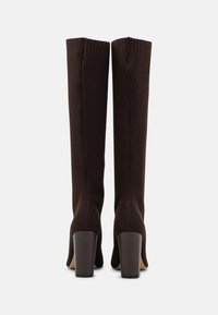 Bottes à hauteur de genou, en tissu marron côtelé, avec une tige large et un talon bloc. Elles présentent un design texturé en maille et une base de talon lisse.