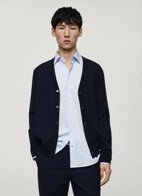 Marinblå cardigan med knappar, lagd över en ljusblå skjorta. Erbjuder en mjuk textur och klassisk passform, vilket framhäver en enkel, modern design.