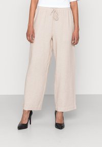 Beige vida byxor med elastisk midjeband och dragsko, tillverkade av mjukt, lättviktigt tyg. Kombineras med svarta klackskor.