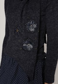 Tmavě šedý svetr s květinovými aplikacemi v námořnické modré a stříbrné barvě, s texturovanou tkaninou, šikmým lemem a zdobenými květinovými detaily.