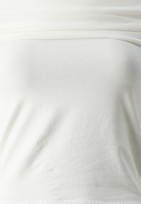 Bela, prilegajoča majica iz mehke bombažne jersey tkanine. Ima gladko teksturo z rahlim raztegnjenjem in okroglim izrezom. Minimalističen dizajn.