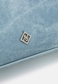 Jasnoniebieska torba z denimu, z fakturowaną powierzchnią i małym srebrnym logo w kwadratowej ramce w rogu. Gładkie krawędzie.