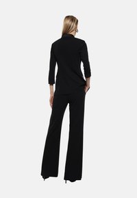 Completo pantalone nero con blazer elegante e pantaloni a gamba larga. Realizzato in tessuto liscio con un design minimalista e maniche a tre quarti.