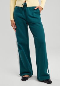 Pantaloni da felpa larghi color teal realizzati in tessuto morbido, con strisce laterali bianche e una vita elastica con lacci.