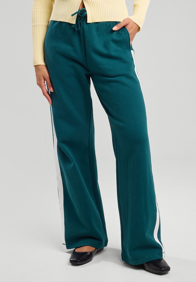 Pantaloni da felpa larghi color teal realizzati in tessuto morbido, con strisce laterali bianche e una vita elastica con lacci.