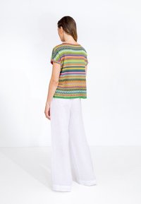 Top a maniche corte con motivi zigzag multicolori, realizzato in tessuto leggero, abbinato a pantaloni larghi in lino bianco.