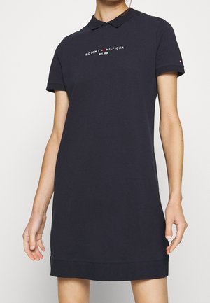 Granatowa sukienka polo Tommy Hilfiger z krótkimi rękawami, kołnierzem i logo na piersi i rękawie, noszona przez osobę.