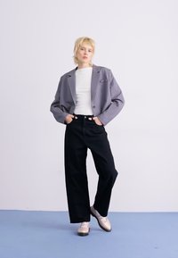 Gray oversized blazer over a white shirt, paired with wide-leg black trousers and light pink shoes. Smooth fabric with minimal detailing.