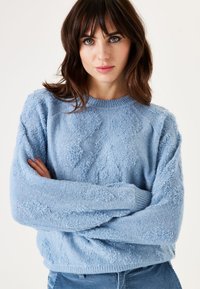 Hellblauer, gestrickter Pullover mit strukturiertem Muster, rundem Halsausschnitt und langen Ärmeln. Weicher Stoff mit einem leicht übergroßen Schnitt.