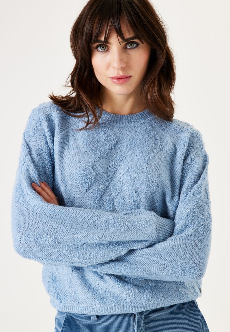 Hellblauer, gestrickter Pullover mit strukturiertem Muster, rundem Halsausschnitt und langen Ärmeln. Weicher Stoff mit einem leicht übergroßen Schnitt.