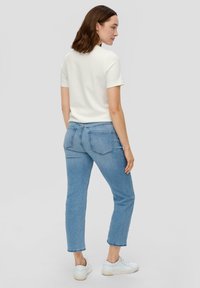 Witte kortemouwen top gecombineerd met lichtblauwe high-waisted jeans. De jeans hebben een rechte snit en subtiele naden op de achterzakken, met witte sneakers.