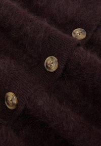 Hnedý vlnený kardigán s jemnou, chlpatou textúrou a veľkými, priesvitnými gombíkmi s jemným vírivým vzorom.