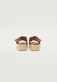 Brown leather espadrille sandals with a woven jute sole, featuring a buckle strap and back support, viewed from the rear.