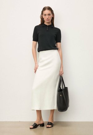 Polo negro de manga corta, falda blanca de longitud media, sandalias negras abiertas y bolso tote negro. Texturas suaves y diseño minimalista.