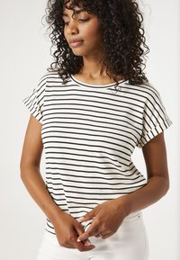 Camiseta de rayas en crema y negro, con mangas cortas enrolladas, cuello redondo y un ajuste holgado. Tela suave y ligera.