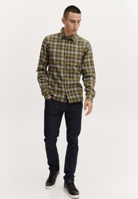 Grønternet skjorte med knapper og lange ærmer, der har hvide striber. Sammen med mørkeblå jeans og sorte sneakers. Glat stofstruktur.