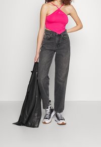 Różowy dopasowany crop top z krzyżującymi się ramiączkami, w zestawieniu z czarnymi dżinsami o wysokim stanie i czarno-białymi trampkami. Na ramionach luźno narzucona czarna skórzana kurtka.