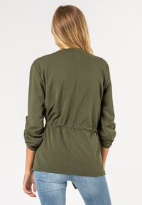 Olijfgroen, lichtgewicht langemouwen top met een gathering bij de taille, ronde halslijn en zachte textuur; achteraanzicht met lichte draping.
