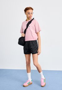 Light pink cropped t-shirt with logo, black shorts with white stripes, pink sneakers with green accents, white socks, and a black shoulder bag.