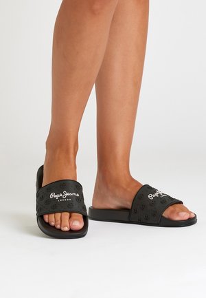 Jalat, joissa on mustat Pepe Jeans Londonin avokkaat liukusandaalit, joissa kohokuvioitu logokuvio valkoisella taustalla.